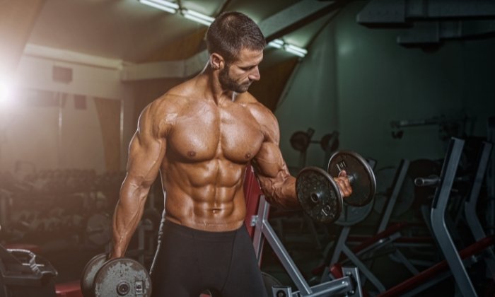 A personal trainer from the area exercises gyms. The photo shows a man about 30 years old in a dark room lifting two dumbbells